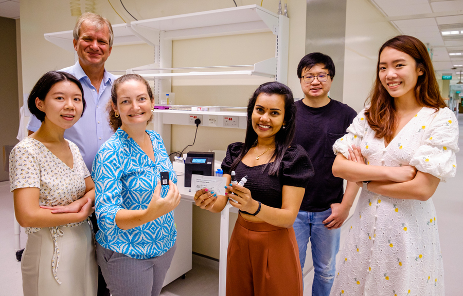 Six researchers pose for a photo holding components of their rapid Covid test kit