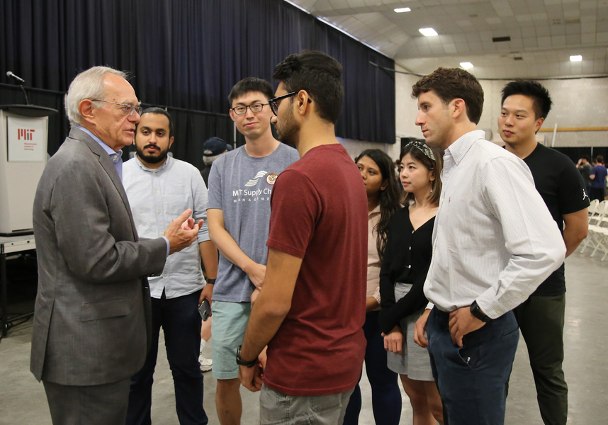 President Reif talks to a group of graduate students. The podium and seating are visible in the background.