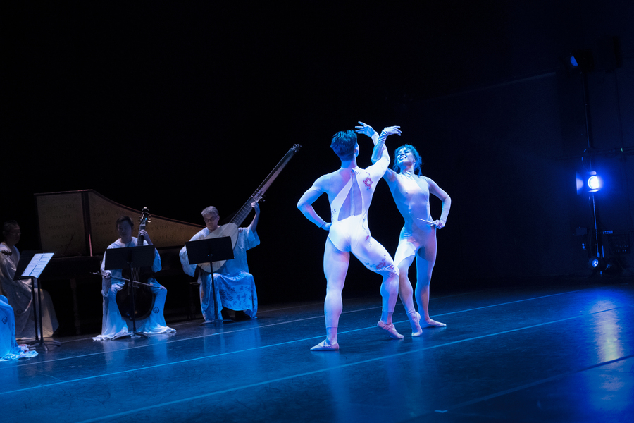 Two ballet dancers with linked arms on a blue-lit stage