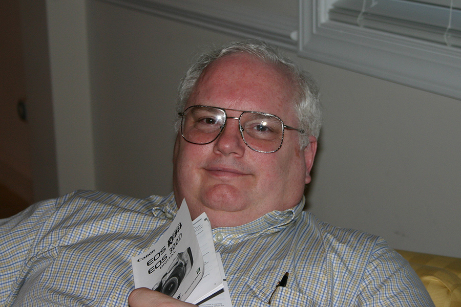Snapshot of Tom Eagar, lounging on a couch, holding a camera instruction booklet