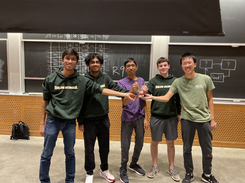 Five participants from the Enloe Magnet High School winning team hold their trophy in front of a chalkboard