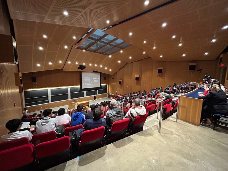 A semi-full audience photographed from the back of Kresge Auditorium. Anka Hu stands onstage.