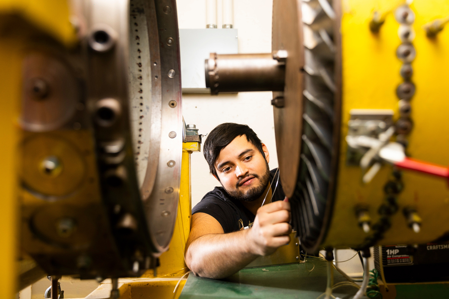 Graduate student Marcos Logrono reaches his arm between two huge parts of a turbofan engine in a laboratory.