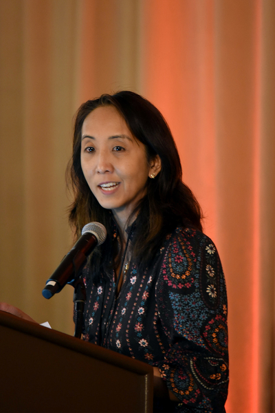 Photo of Eileen Tanghal standing at a podium and speaking into a microphone.