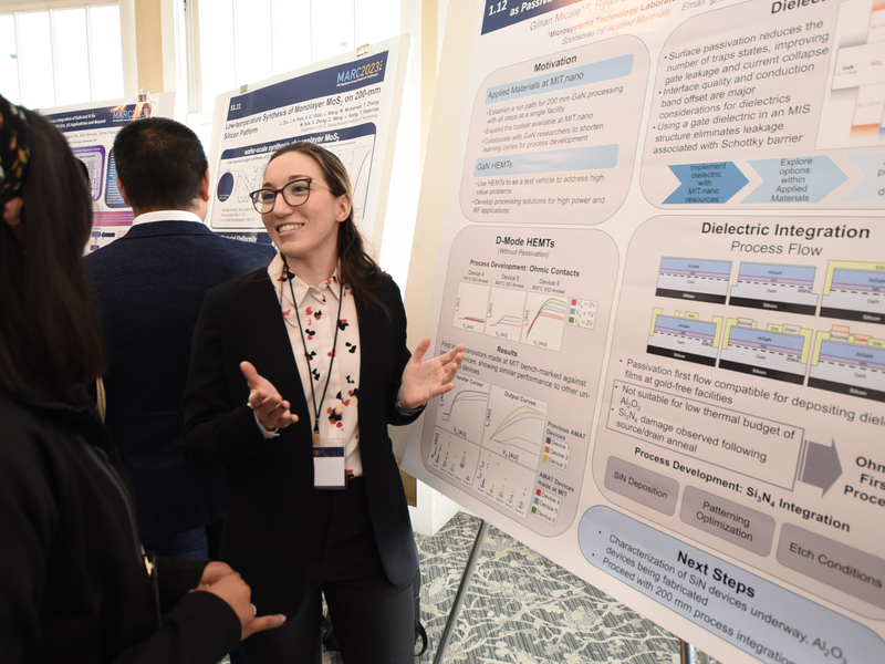 Gillian Micale gestures in front of a poster with dense charts and diagrams explaining her research.
