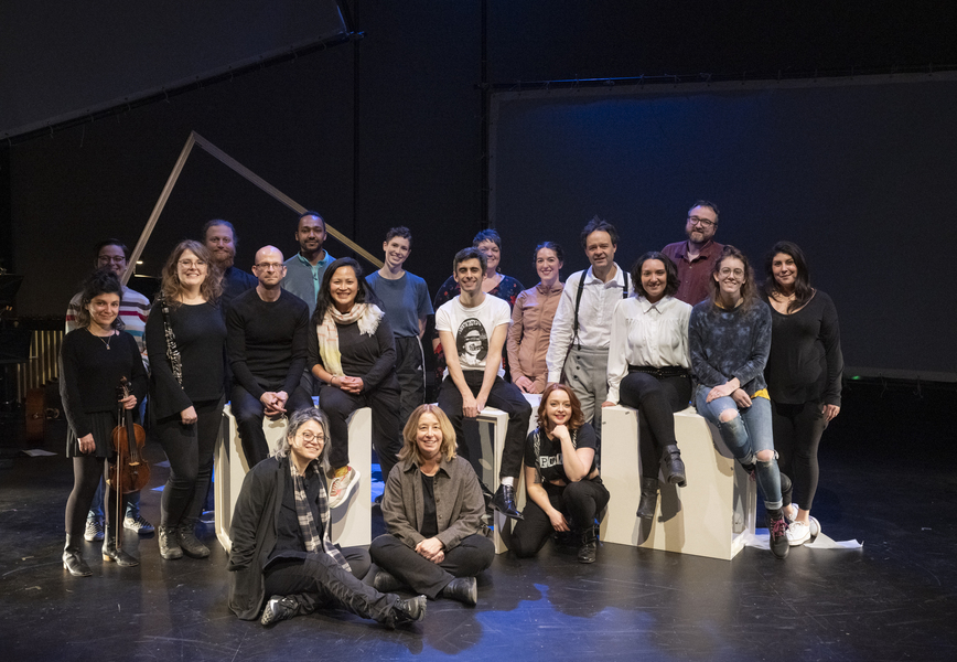 Team photo of 19 creators and performers on a stage