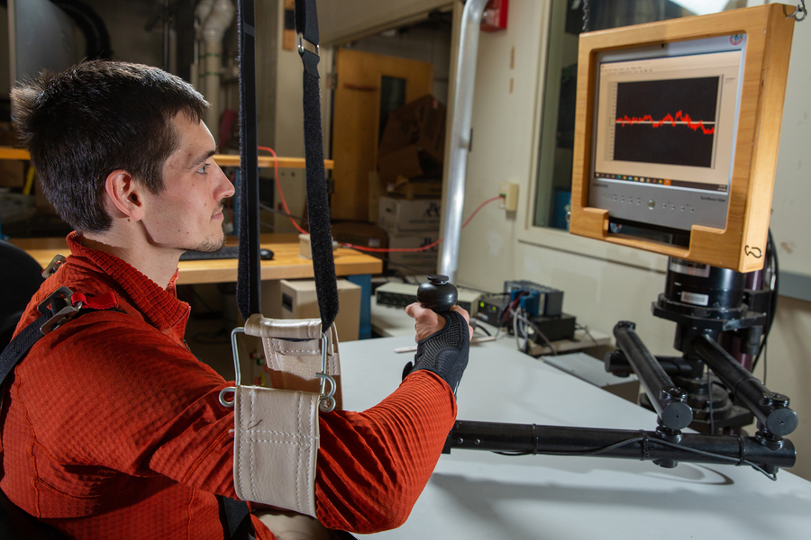 Hermus looks at a computer display while his arm is in a sling. He grips a joystick while wearing a black wrist strap.