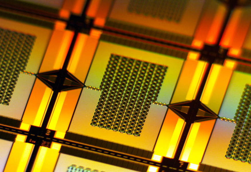 A yellow-lit closeup zooms in on one tiny, rectangular amplifier on the wafer. It has a chain-like rectangular grid in center that connects to the left and right edges of the wafer.