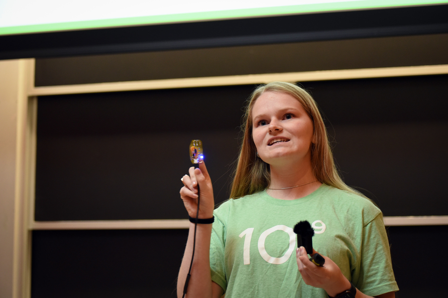 A student at the front of the lecture hall holds up a small electronic device clipped to her index finger.