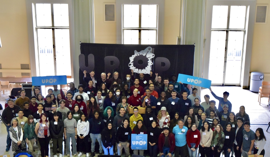 The full, very large group of students and mentors standing and smiling inside Walker Memorial, holding UPOP signs.