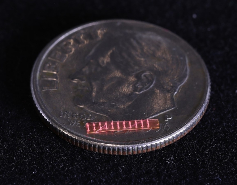 Image of a red microneedle array on a U.S. dime. The array is a small fraction of the area of the coin.