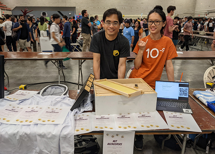 Michael Gilbert and Kerlina Liu stand behind a table displaying beekeeping materials in a crowded auditorium