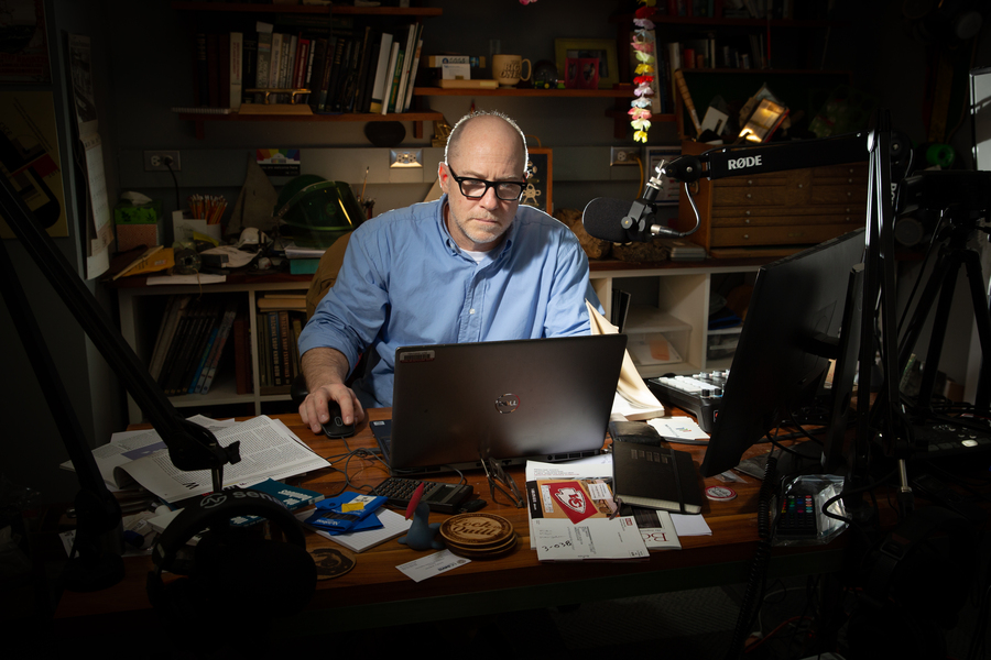 Danny Braunstein, sitting in a pool of light in an otherwise-dim room, looks at a laptop. There is a professional-grade boom microphone in front of him.