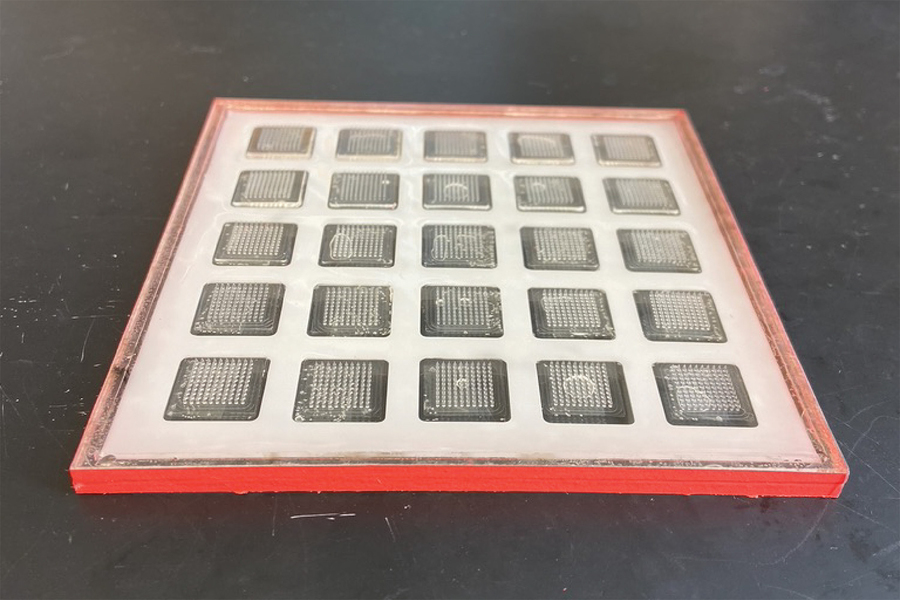 Photo of the mold inside a red frame. The mold is white and has a 5x5 grid of squares. The squares are translucent and each have a grid of microneedles on them.