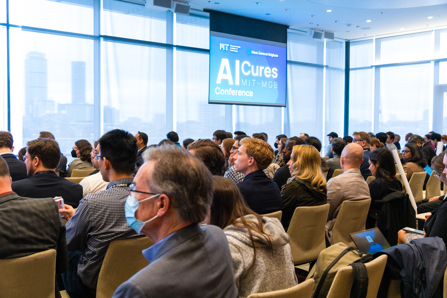 Photo overlooking an audience with "MIT-MGB AI Cures" displayed on the screen at the front.