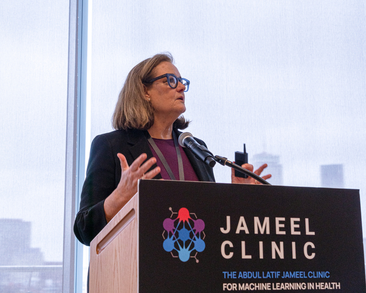 Close-up shot of Kate Walsh speaking at a lectern that reads "Jameel Clinic" in front.