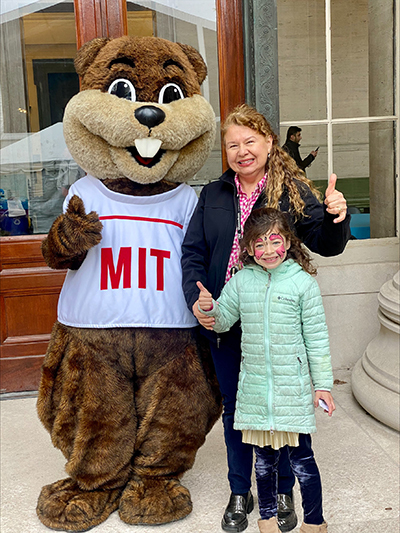 MIT mascot Tim the Beaver poses with Sally Romero and a child, all of them giving a thumbs up