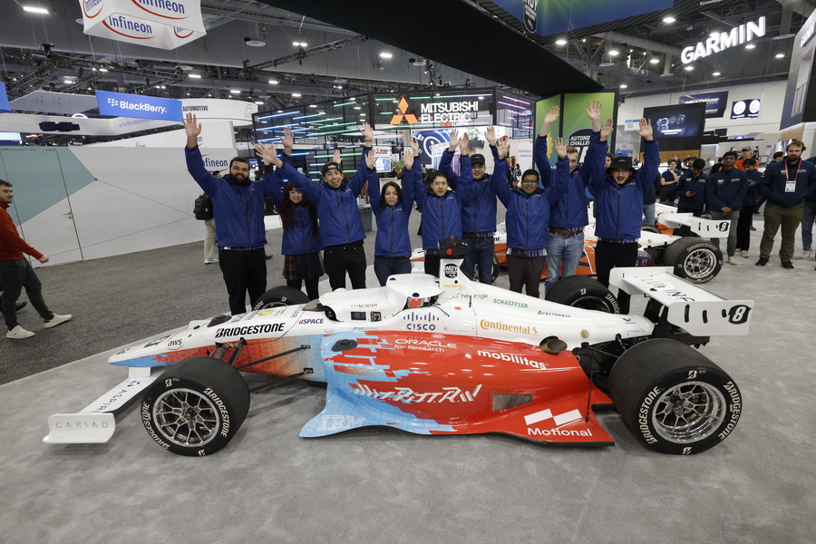 Nine people stand in a line behind their driverless race car, their hands raised in the air