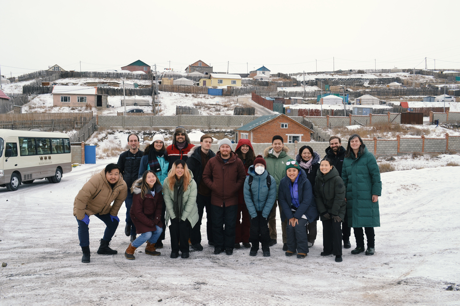 15 students and faculty pose for a group photo in front of a snow-dusted residential gers