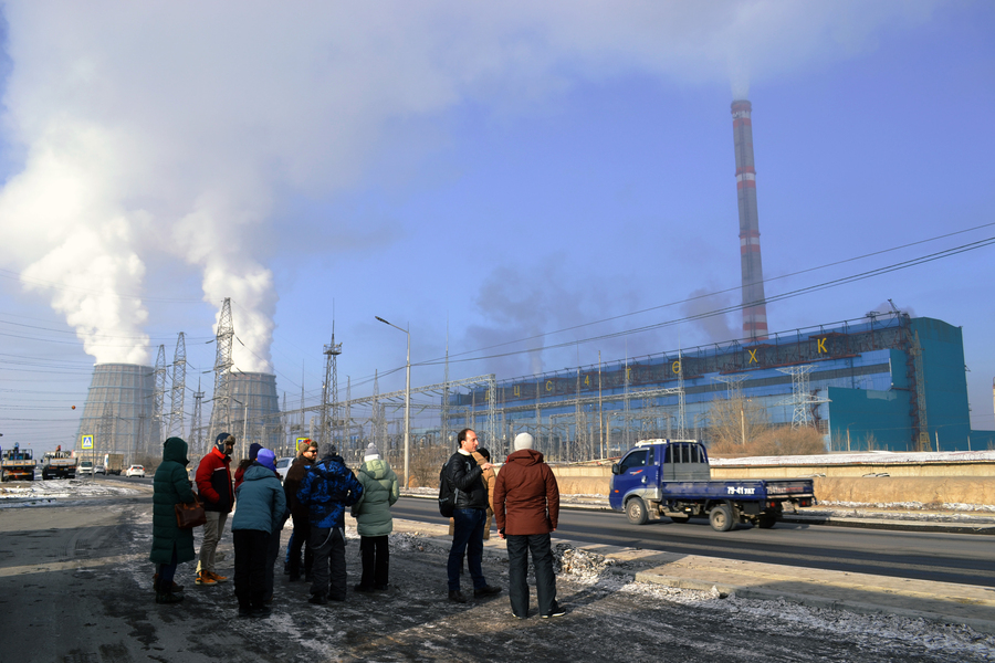 Students and faculty in winter jackets gaze up at one of Ulaanbaatar’s largest coal-fired power plants, emitting smoke.