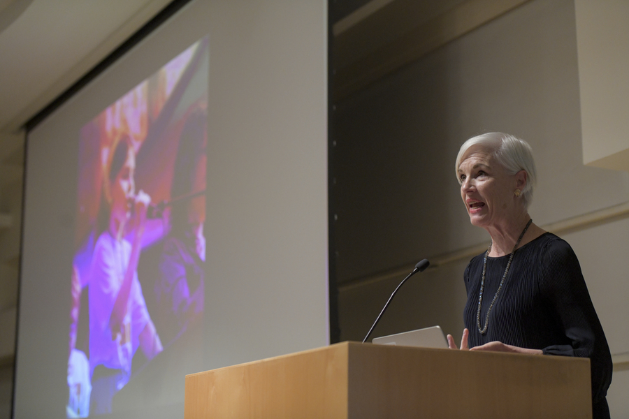 Cecile Richards stands behind a lecturn, speaking into the microphone. On the auditorium screen to her left is a picture of a young girl addressing an unseen crowd