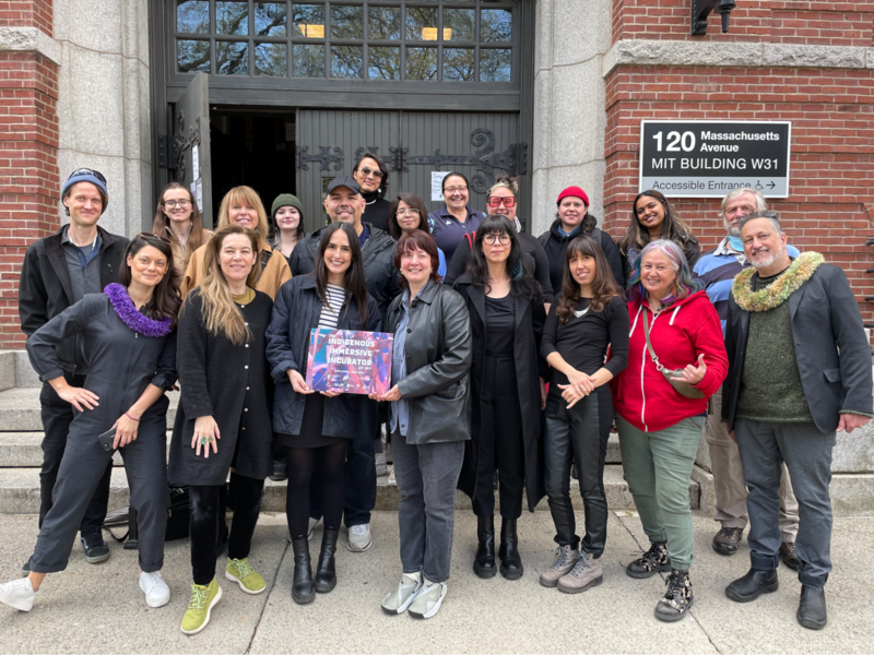 20 people pose for a group photo in front of large doors and sign reading MIT Building W31
