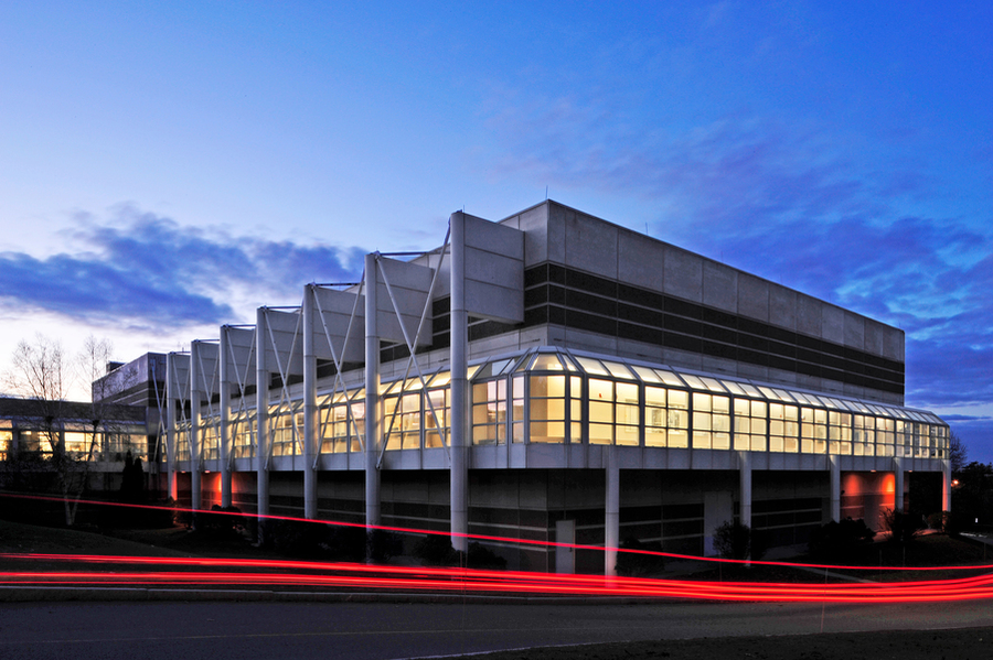 An exterior shot of the Microelectronics Laboratory building at dusk; a long-exposure technique creates a red streak from the tail lights of passing cars.