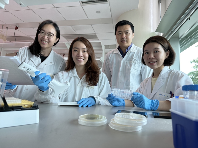 Four researchers in white lab coats and blue nitrile gloves pose at a bench