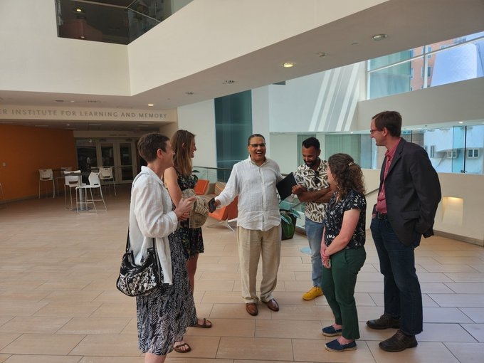 Six people standing in a semicircle at the Picower Institute, laughing.