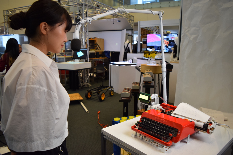 Kyung Yun Choi, seen in profile, speaks into a boom microphone attached to a red typewriter inside a lab space