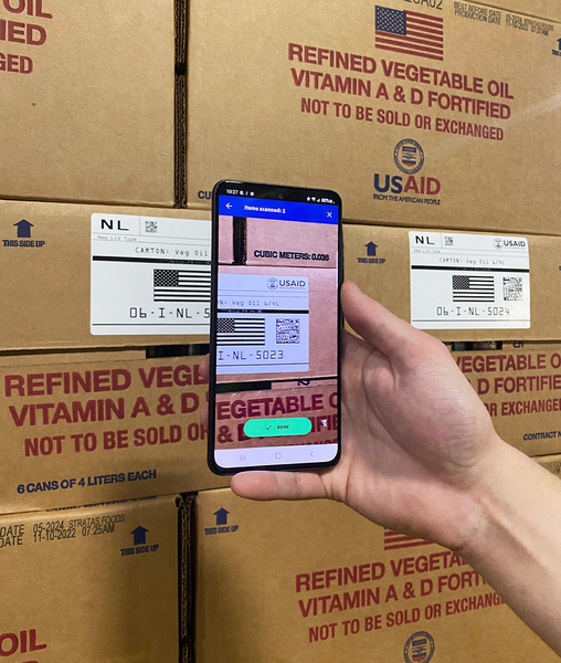 Closeup of a hand holding a smartphone, scanning a barcode on a carton of vegetable oil.