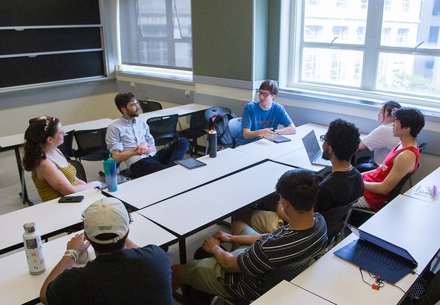 Six students and Associate Professor Justin Khoo sit around a table and listen as Quincy Cantu speaks.