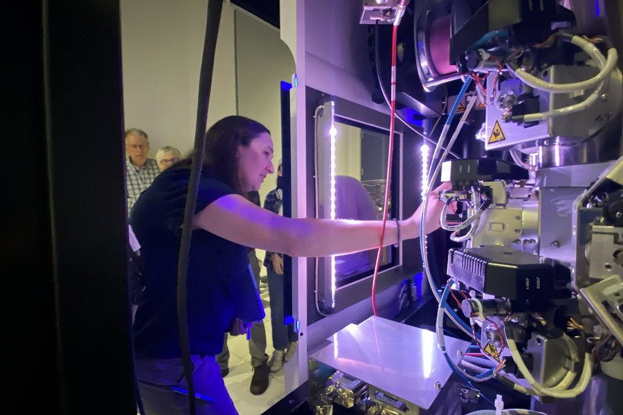 Sarah Sterling reaches her arm into a tangle of wires and metal parts inside a large microscope instrument.