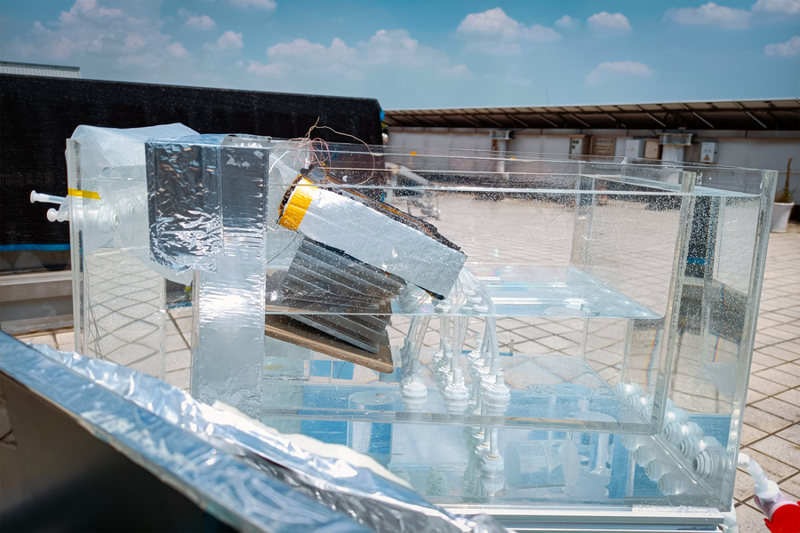 A desalinization prototype setup, a clear rectangular box with waters, tubes, and square spring surrounded by a larger rectangular box, outside in the sun