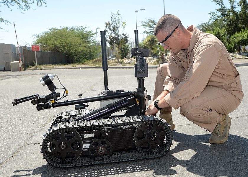 A disposal technician in a jumpsuit makes adjustments to a small, tanklike robotic vehicle