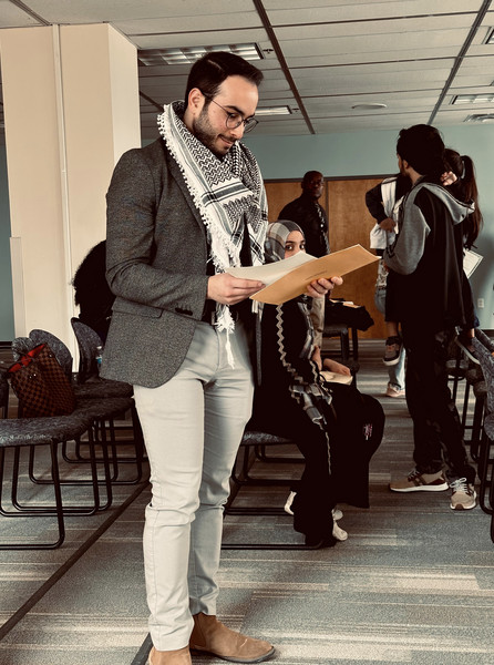 A man in a suit, a keffiyeh loose around his neck, receives an award from a woman on stage. 