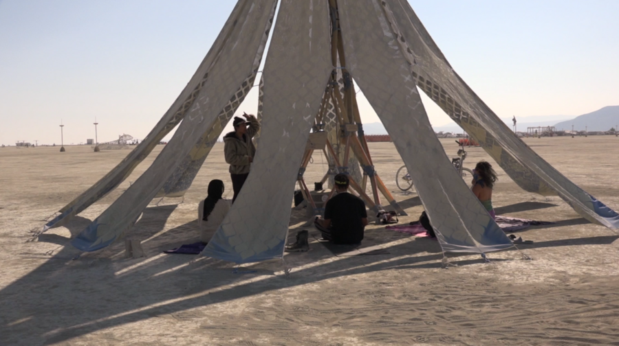 People seen through the gaps in draped fabric pieces of the Living Knitwork Pavilion participate in a yoga session.