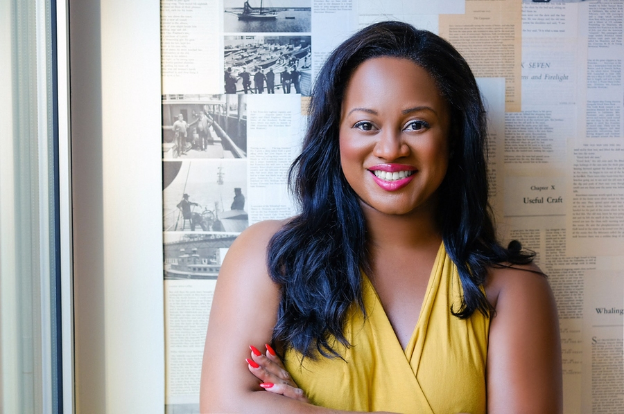 Headshot of Adonica Shaw, posing while standing in front of a bulletin board