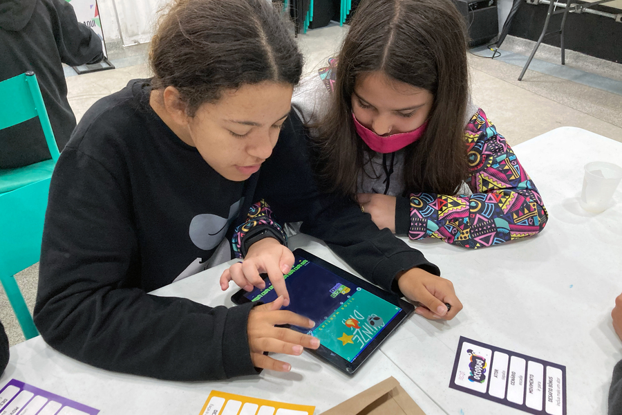 Two children at a table share a tablet computer. 
