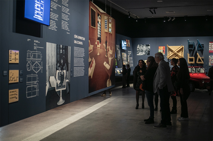 Several people in a dimly lit exhibit hall stop to read a panel at the exhibit's grand opening.