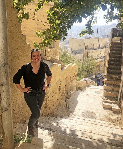 Elizabeth Parker-Magyar poses at the top of an ancient-looking stone staircase overlooking many old buildings in Amman, Jordan