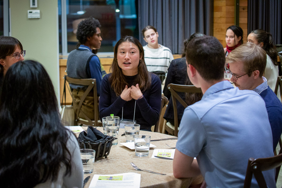 Five people sit around a dinner table, listening to one speak. Another table can be seen behind them.