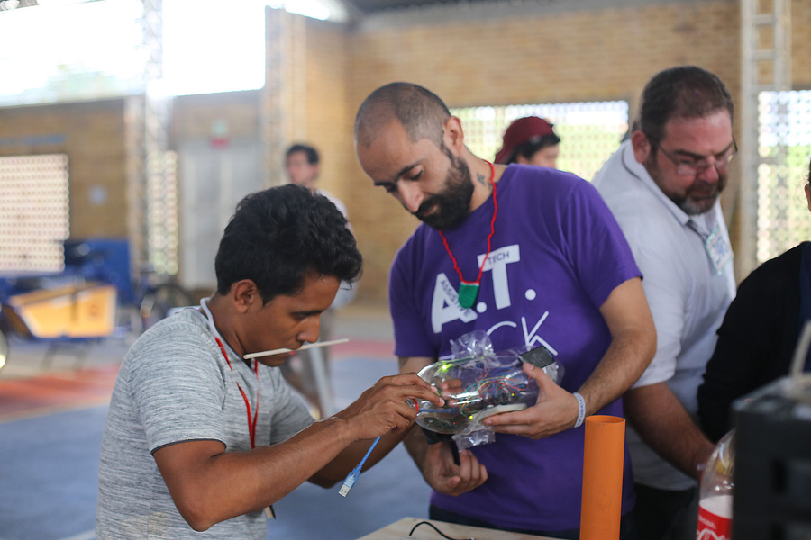 Pedro Reynolds-Cuéllar and another man hold a plastic bottle containing electronics in an indoor space.