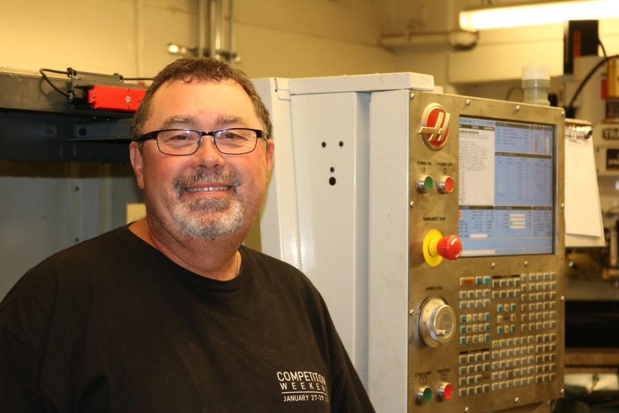 Pat McAtamney smiles in front of a large machine inside a cement brick room