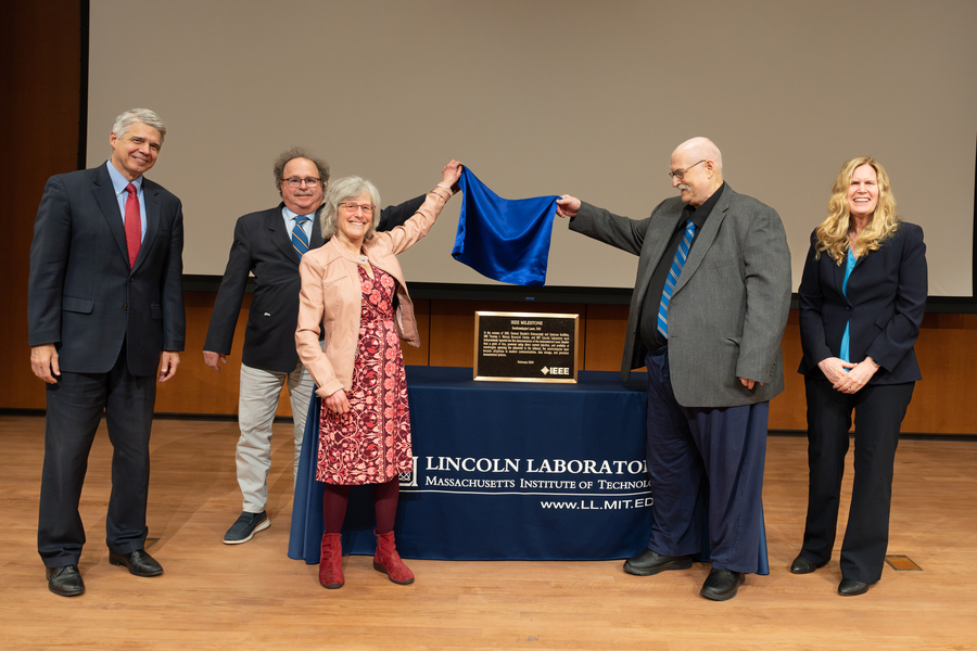 A group of people smile as they take the covering of an award plaque on a table.