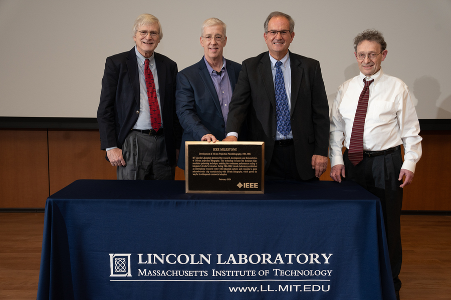 David Shaver, Dan Corliss, Craig Keast, and Mordechai Rothschild stand around a table with the 193 nm photolithography plaque.