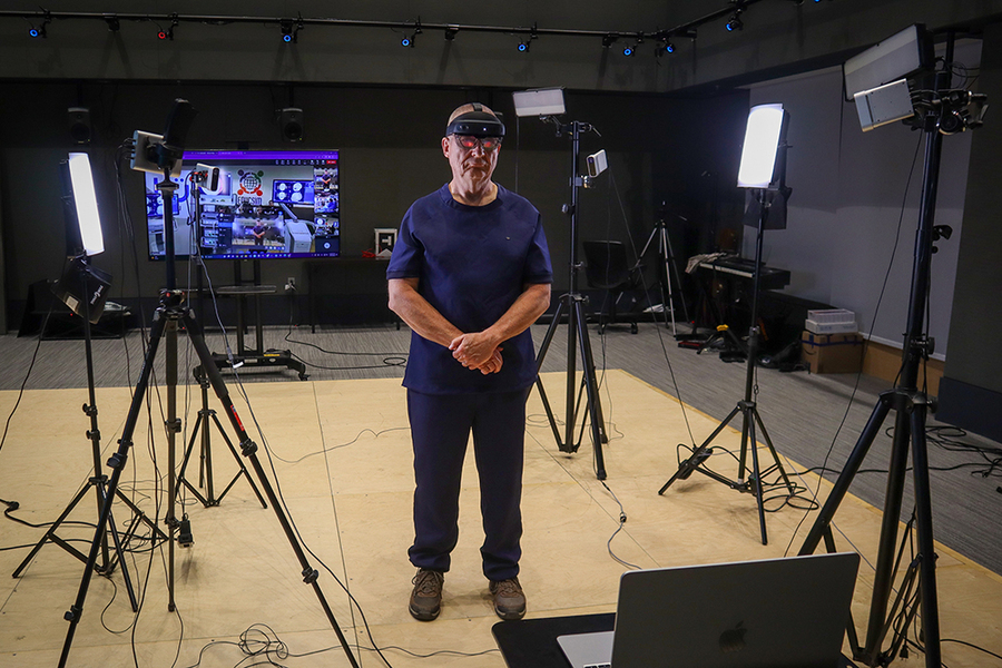Benjamin Warf, weaering VR goggles, stands amid light stands, cameras, a laptop, and other equipment.