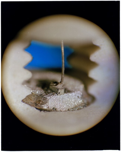 Close-up photo of a semiconductor laser shows a tiny block of a metallic material, with a wire attached to it.