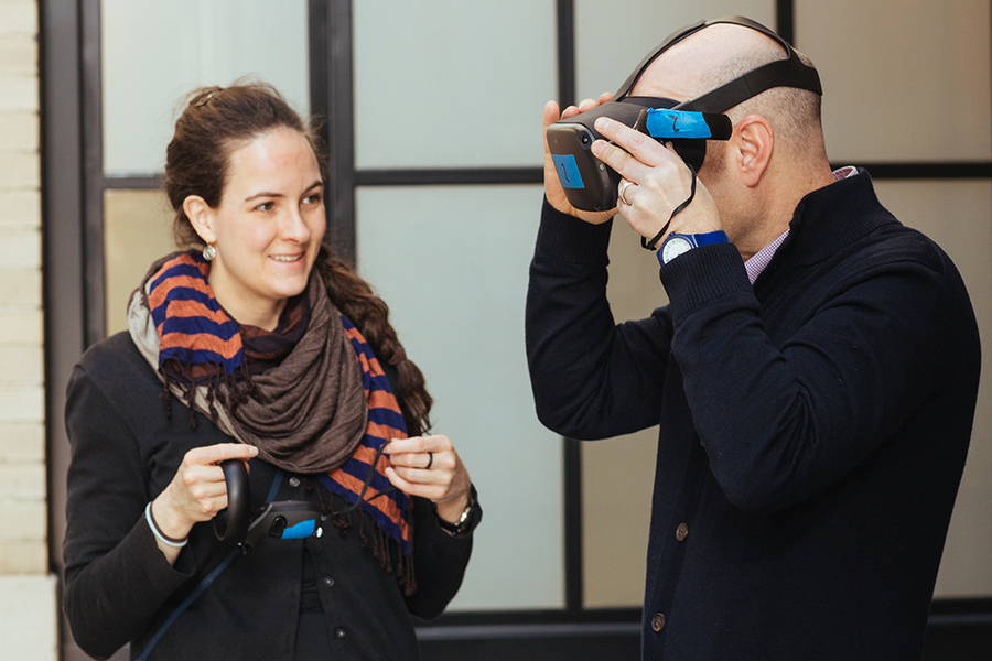 Lydia Brosnahan and an unidentified man stand in front of a window; the man is wearing a virtual reality headset.