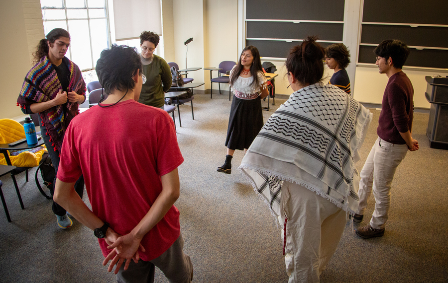 Seven people stand in a circle in a classroom. Soledad Chango, at center, wears a traditional Ecuadorian dress